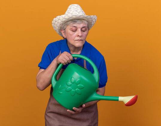 女自信的上了年纪的女园丁戴着园艺帽拿着水壶看着浇水穿帽子