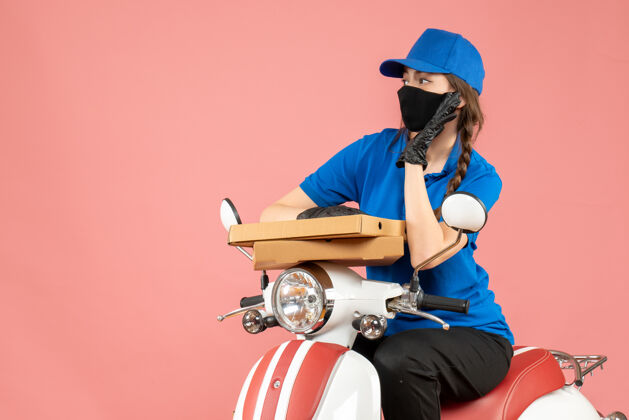 坐俯视图：年轻的女快递员戴着医用口罩和手套坐在滑板车上 用粉彩桃子传递订单运动滑板车粉彩