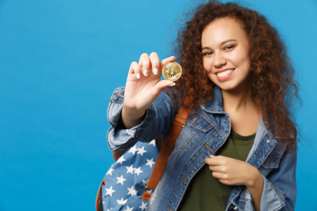 投资年轻的非裔美国少女 穿着牛仔服 背包里装着比特币 孤零零地站在蓝色的墙上银行包商业