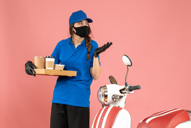 工人顶视图好奇的信使女孩戴着医用口罩手套站在摩托车旁边拿着咖啡小蛋糕粉彩桃红色背景摩托车小人