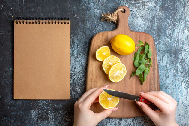 黑板俯瞰图一个手切碎新鲜柠檬和薄荷在木制砧板旁边的螺旋笔记本在黑暗的背景背景蔬菜木材