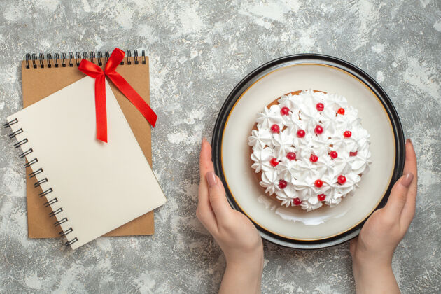 背景上图：手拿着一个盘子 上面放着美味的奶油蛋糕 蛋糕上装饰着水果和笔记本 背景是冰冰新鲜碗