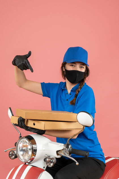 人年轻自信的女快递员戴着医用口罩和手套拿着粉彩桃色盒子的垂直视图人工作专业