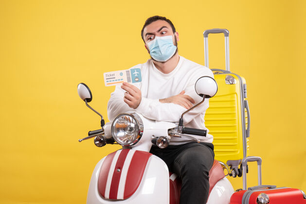 人旅行概念的俯视图 戴着医用面罩的年轻人坐在摩托车上 黄色手提箱放在上面 拿着车票感到震惊面具感情抱
