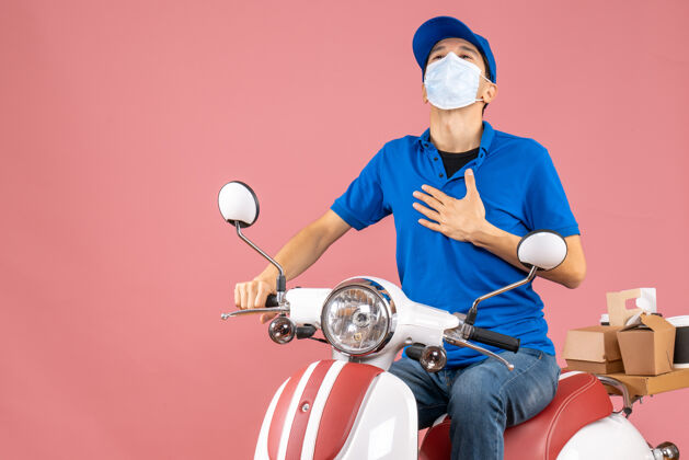 面具俯视图：戴着医用面罩戴着帽子的快递员坐在滑板车上 在柔和的桃色背景下感到自豪摩托车医学滑板车