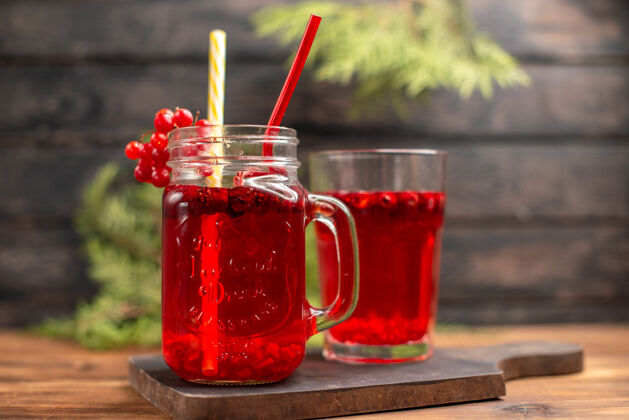 木头特写镜头中的新鲜葡萄干汁在一个玻璃杯和一个杯子与一个木制砧板管服务冰茶玻璃