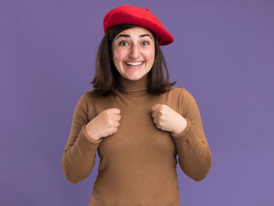 年轻一个戴着贝雷帽的年轻漂亮白人女孩兴奋地把拳头放在胸前紫色胸部贝雷帽