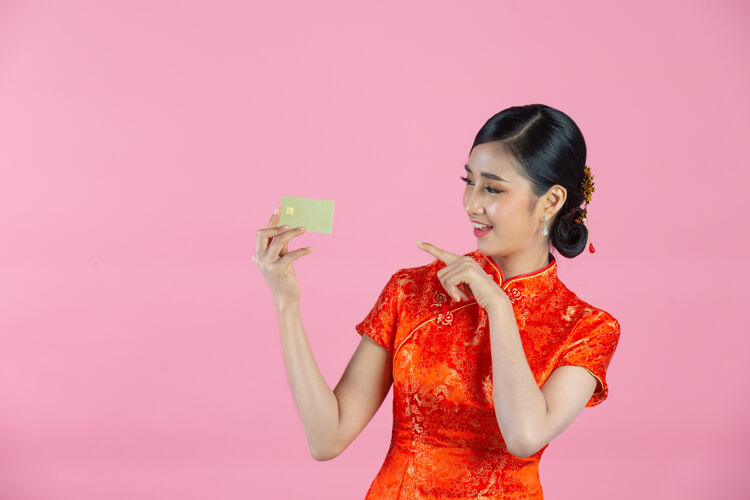 女人美丽的亚洲女人开心的微笑 在粉色背景上展示中国新年的信用卡亚洲年轻问候语