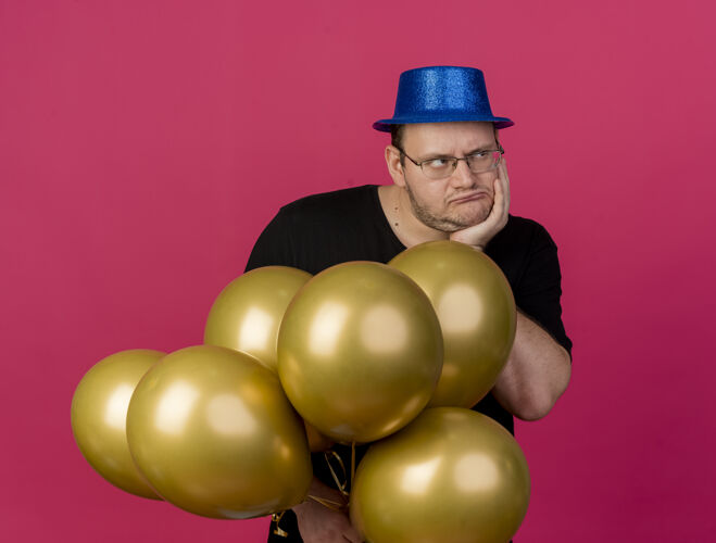 手一个戴着眼镜 戴着蓝色派对帽 手放在下巴上 手里拿着氦气球的未获释的成年斯拉夫人站在一旁看着穿举行空间