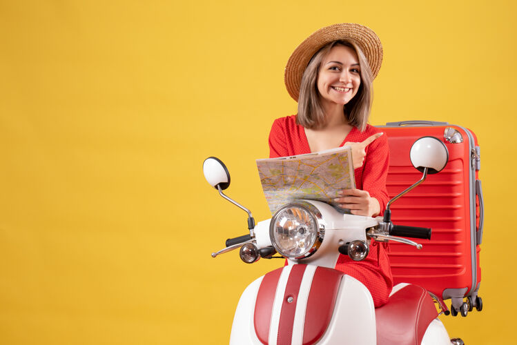 漂亮女孩骑着轻便摩托车的漂亮女孩拿着地图指着她的手提箱车辆剪影手提箱