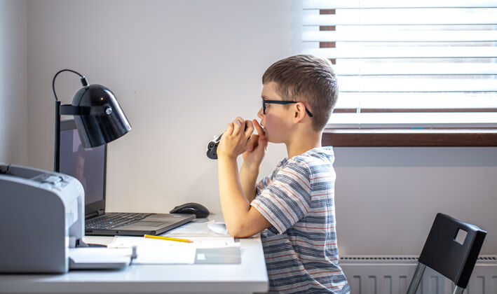 视频通话一名小学生坐在笔记本电脑前的桌子旁 在家里通过视频链接进行在线交流教育房间拿着
