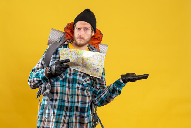 服装迷惑不解的年轻游客带着皮手套和背包拿着地图人地图帽子