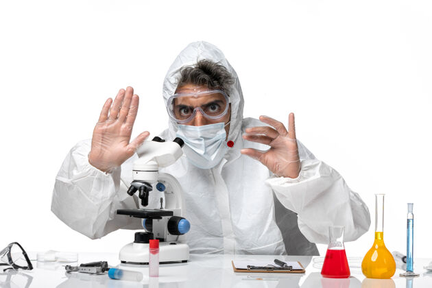 显微镜男医生穿着防护服 带着无菌口罩 用显微镜观察浅白色使用绝育大流行