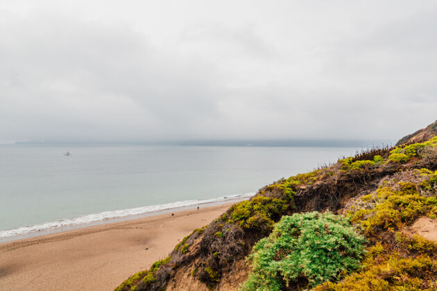 自然海滩四周是岩石 大海笼罩在多云的天空下的雾中阴暗草地海洋
