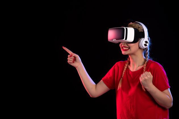 正面戴着耳机在黑暗的墙上玩虚拟现实的年轻女士的正视图耳机人物成人