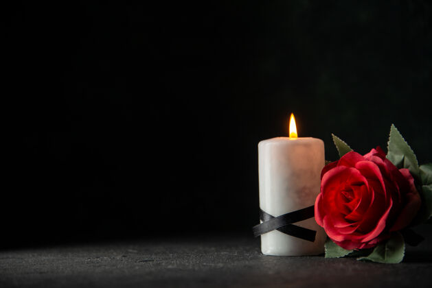 前面在黑暗的墙上 白色的蜡烛和红色的花朵的正面视图燃烧打蜡白色蜡烛