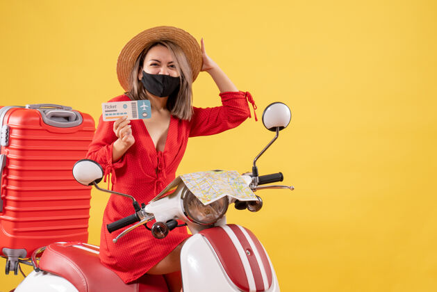 摩托车戴着黑色口罩的年轻女士高兴地坐在轻便摩托车上 手里拿着红色的手提箱 手里拿着车票票红色车辆