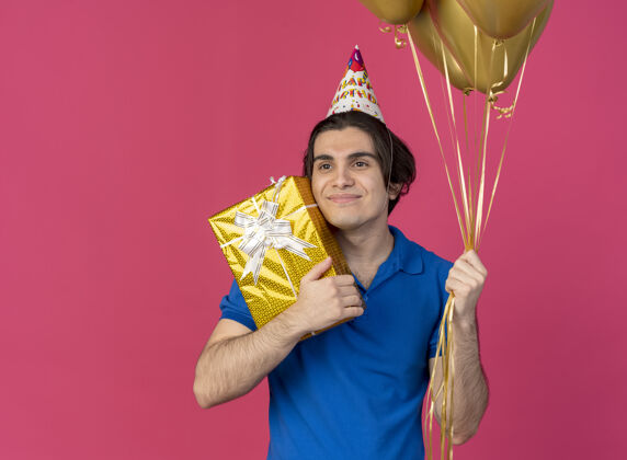 男人帅气的白种人戴着生日帽 手里拿着氦气球和礼盒看着身边盒子氦气粉色