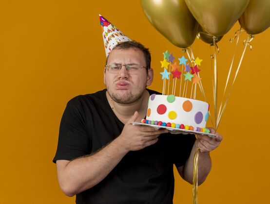 蛋糕贪婪的成年斯拉夫人戴着眼镜 戴着生日帽 伸出舌头 手里拿着氦气球和生日蛋糕成人卡住光学
