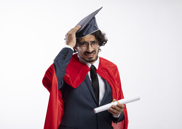 红色失望的年轻白种人超级英雄戴着眼镜 穿着红色斗篷的西装 手拿毕业帽 手里拿着毕业证书眼镜毕业西装