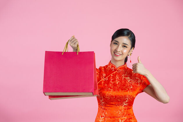 服装美丽的亚洲女人快乐的微笑和购物在中国新年的粉红色背景红色亚洲微笑