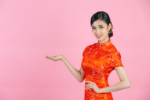中国人美丽的亚洲女人快乐的微笑 在中国新年的粉红色背景上向你展示一些东西年红色复制空间