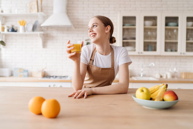 素食年轻漂亮的女人在厨房里围着围裙 水果和橙汁冰沙女人有机