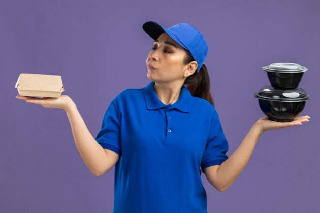 送货身穿蓝色制服 头戴鸭舌帽的年轻女送货员站在紫色的墙上 手里拿着食品包 看上去很困惑 没有回答女人制服站着