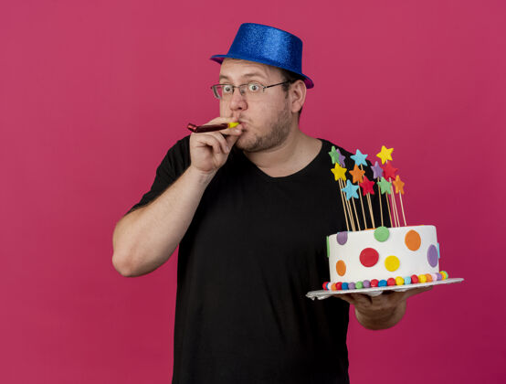 粉色惊讶的成年斯拉夫人戴着眼镜戴着蓝色派对帽拿着生日蛋糕吹派对哨子帽子复制空格
