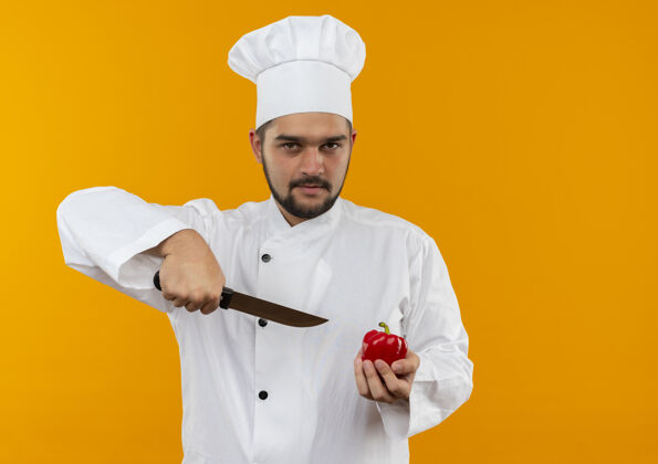 烹饪自信的年轻男性厨师身着厨师制服 手拿胡椒粉和刀 隔离在橙色的墙上 留有复印空间信心胡椒制服