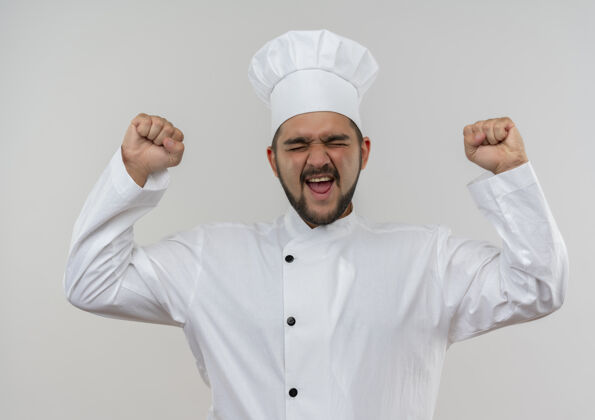 厨师快乐的年轻男厨师穿着厨师制服举起拳头闭上眼睛隔离在白墙上制服欢乐提高