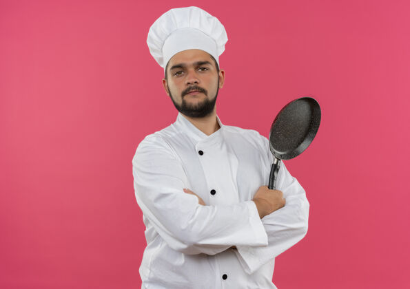 姿态自信的年轻男性厨师 身着厨师制服 站着 姿势封闭 手拿煎锅 隔离在粉色墙壁上 留有复印空间信心烹饪男性
