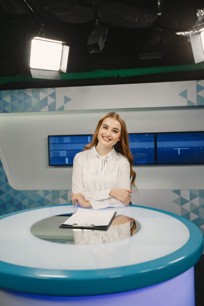 采访电视节目正在演播室准备新的广播节目穿着白衬衫的微笑女孩坐在桌子旁主播电视麦克风