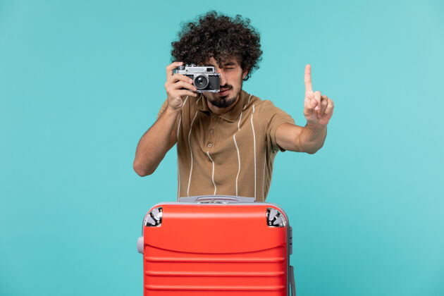 脸带着红色手提箱的度假男人在蓝色地板上用相机拍照旅行飞机度假海上旅行旅行人手提箱肖像