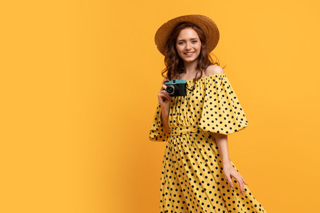 温暖戴草帽 穿夏装的旅行妇女在黄色的背景下与复古相机合影喜悦优雅时尚