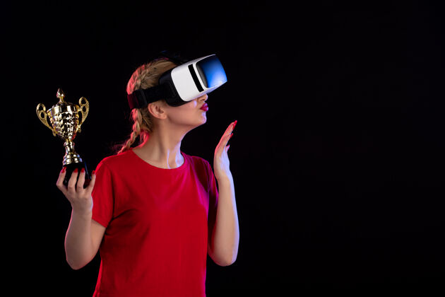 年轻女性年轻女子在黑暗的墙上玩vr和赢得奖杯的正面图赢家虚拟现实游戏