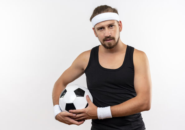 足球自信的年轻帅气的运动型男人戴着头带和手环拿着足球 在白色的墙壁上显得孤立无援腕带男人佩戴