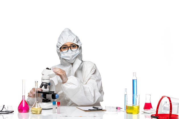 特殊前视图穿着特殊防护服的年轻女化学家正在用显微镜观察浅白色背景的化学实验室病毒人化学实验室外套