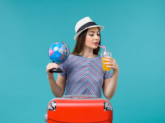 旅行正面图：度假中的女人拿着果汁和地球仪在蓝色的背景海上航行度假暑假旅行果汁世界旅程