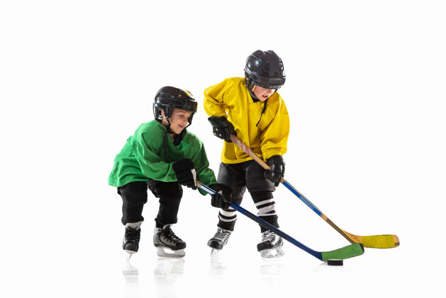 头盔冰球场上拿着棍子的小冰球运动员和白色的工作室墙装备孩子动作