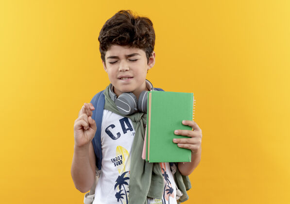 耳机小男孩戴着书包 戴着耳机 抱着书 双手交叉着手指 眼睛紧闭着背举行穿
