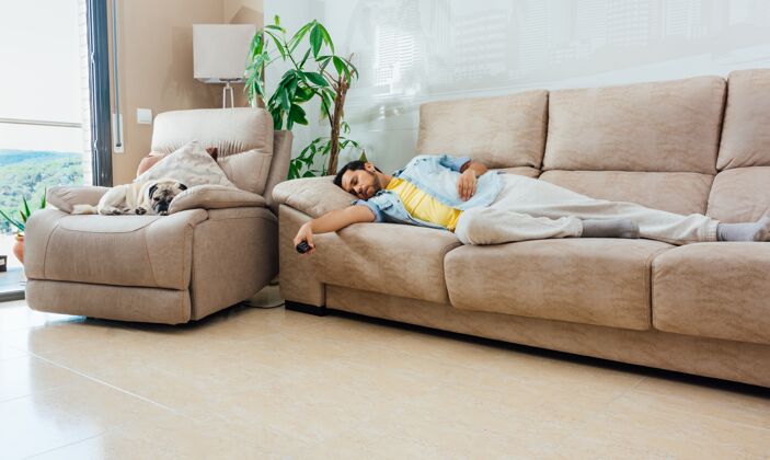 电脑一个穿着休闲服的年轻人 手里拿着电视遥控器 睡在家里的沙发上休闲男人远程