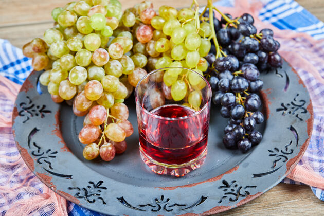 深色一束葡萄和一杯果汁放在陶瓷盘子里 还有桌布串绿色葡萄
