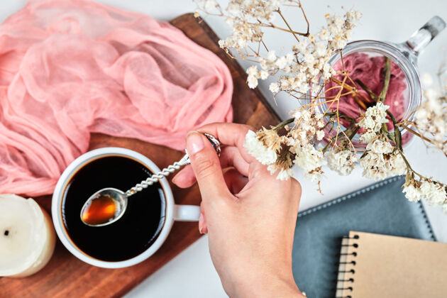 顶视图手拿一杯咖啡放在木板上 上面放着蜡烛 桌布和鲜花木头自然浓缩咖啡