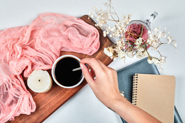 咖啡手拿一杯咖啡放在木板上 上面放着蜡烛 桌布和鲜花杯子浓缩咖啡自然