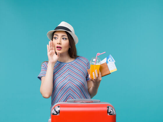 旅行正面图：度假中的女人拿着她的红包拿着机票和果汁在蓝色的地板上旅行票女人