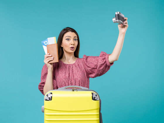 拿着前视图年轻女子手持相机在度假途中拍摄蓝色背景的旅行度假女子出海漂亮抱着相机