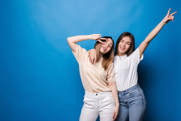 笑永远的朋友两个戴着太阳镜的可爱女孩在蓝色的墙上微笑着摆姿势夏天魅力微笑