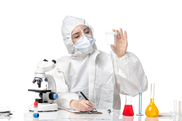 保温瓶正面图：年轻女医生穿着防护服 戴着口罩 因为白色桌子上有一个装着柯维德病毒的瓶子药病毒外套
