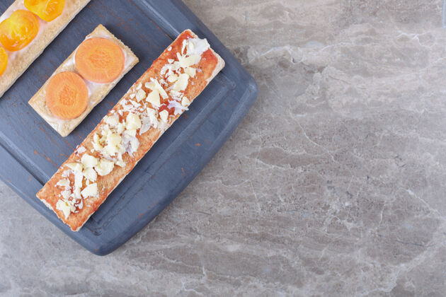 美味把胡萝卜 奶酪和西红柿片放在松脆的面包上 放在木制托盘上 放在大理石表面风味大米奶酪